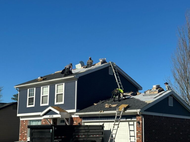 Roofers installing dark shingles on two-story blue home