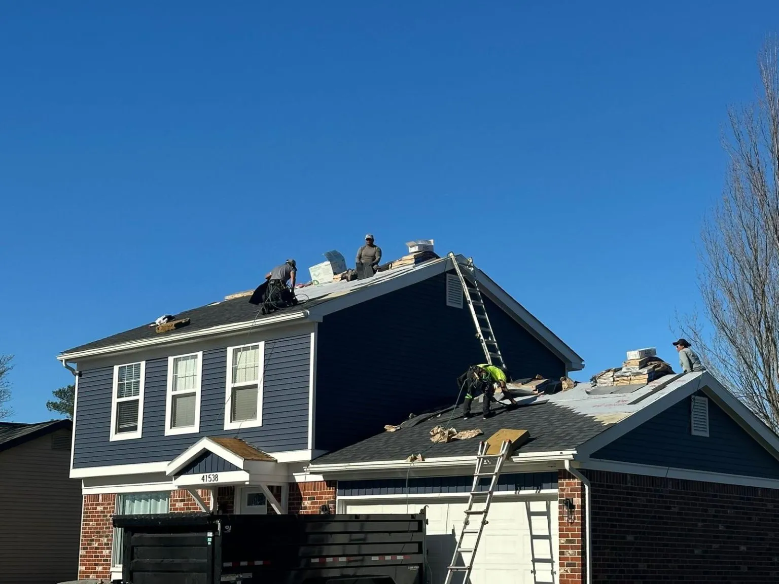 Roofers on ladders installing shingles on blue two-story home