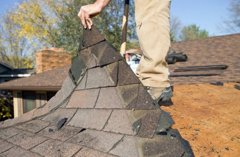 Roofer tearing off old damaged asphalt shingles from roof